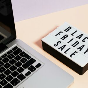 A laptop beside a lightbox sign with 'Black Friday Sale' for online shopping promotions.