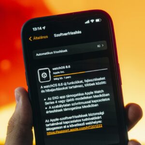 Hand holding a smartphone displaying WatchOS 8.6 update notification against warm gradient background.
